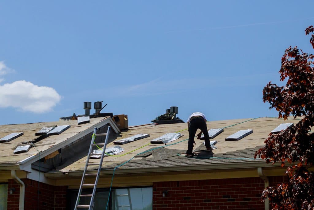 Roof repair, worker with replacing gray tiles shingles on house being applied