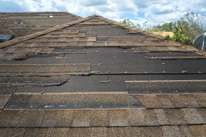 Damaged house roof with missing shingles after hurricane. Consequences of natural disaster.